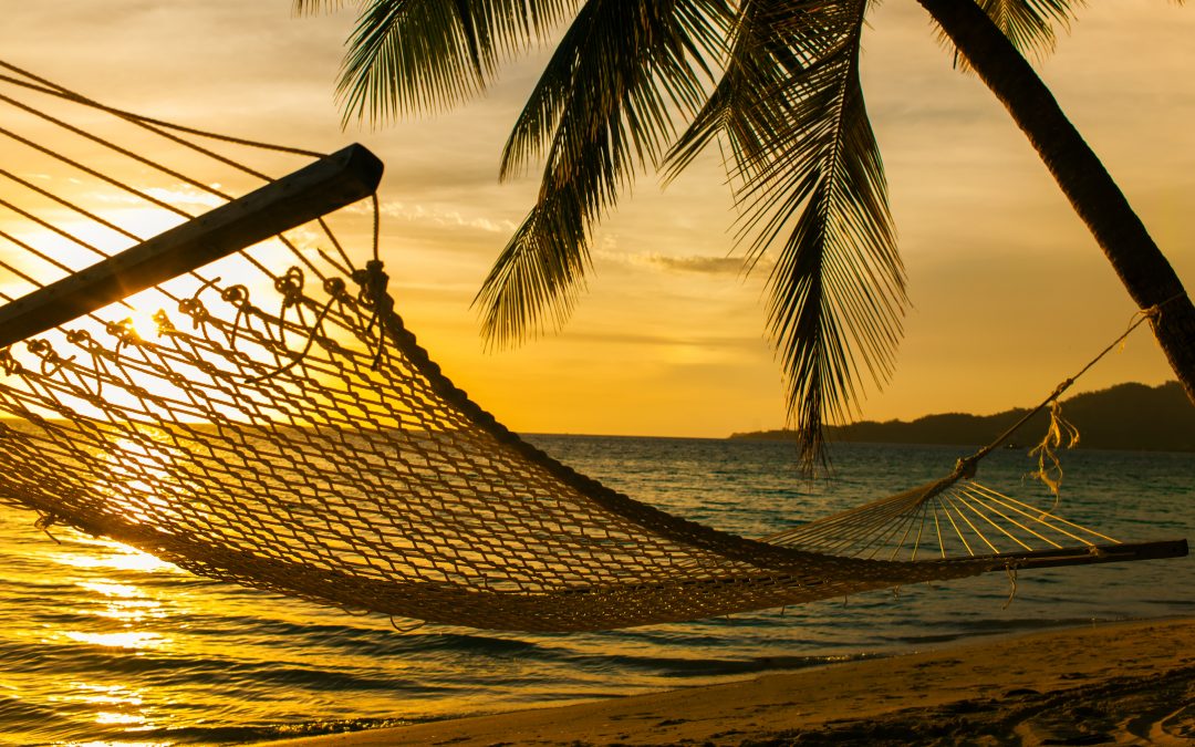An empty hammock hangs in front of a sunset